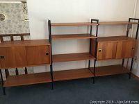 Front view showing three vertical black metal supports, five teak shelves and two enclosed cabinet modules