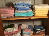 Multiple stacks of assorted towels in pastel and neutral colors on wooden shelves.