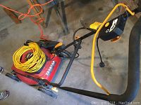 Red Homelite electric lawn mower with yellow extension cord coiled on top