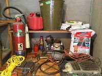 Wide view of the lot showing large items: fire extinguisher, fuel container, bucket, bags of ice melt, trouble light, various tools spread on wooden surface.
