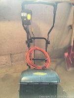 Front view of Yardworks electric snow thrower showing control handle with attached orange extension cord coiled up.