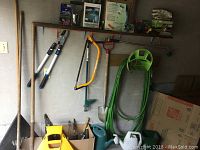 Wide view of gardening tools hanging on wall and garden hose on reel with watering cans on the floor.