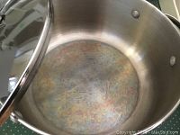 Close-up photo of a large stainless steel cooking pot interior showing discoloration and light wear