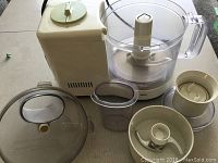 Motobase with large clear processing bowl and various attachments including blades, chopper, and blender.