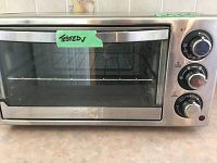 Front view of Oster toaster oven with tested sticker on glass door showing interior wire rack and crumb tray.