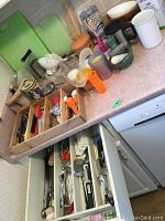 Photo showing kitchen counter and drawers with assorted knives, cutting boards, wooden bowls, and other kitchen items.