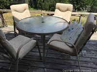 Full set showing round glass-top table and four cushioned chairs outdoors.