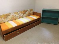 Front view of teak daybed featuring floral and striped cushions with pull-out drawer partially open underneath.