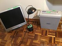 17 inch silver Fuse monitor, black adjustable neck desk lamp, and Brinks paper shredder positioned on the floor.