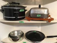 Hamilton Beach slow cooker, electric fry pan on wooden stand, KitchenAid nonstick frying pan, and two springform pans without bases.
