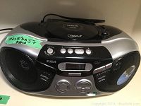 Front view of RCA portable boombox showing speaker grills, control buttons, LCD display, and volume/tuning dials.