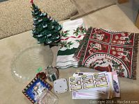 Overall displayed lot contents including ceramic tree, fabric napkins, glass plates, holiday trays, and small decorative items.
