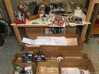 Overview of multiple cardboard boxes containing remote control airplane parts, plans, and materials on floor and table