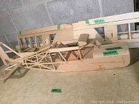 Full length view of wooden lightweight model airplane frame showing fuselage, open framework cockpit area, and wing shell with ribs.