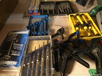 Close-up of small clamps, drill bits, and hand tools with packaging visible