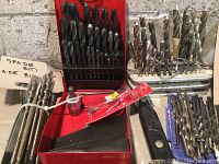 Photo showing metal drill bits in two racks, red toolbox partially visible with small metal parts and files.
