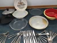 Photo showing 2 clear Pyrex glass baking dishes, 1 Glasbake pie plate, 1 Dr Oetker metal flan pan with ridged edge, and 3 colored plastic bowls (red, yellow, off-white) plus cutlery spread out