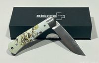 Knife open resting on box, showing full blade and handle artwork