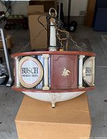 Full view of Busch electric hanging sign with faux wood frame, logo panels, frosted bowl and chain