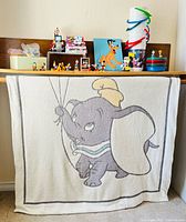Overall lot showing Dumbo throw, figurines, puzzle, washcloths, sealed toys, cups and trays