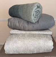 Stacked bedding pieces: rolled throw, comforter, folded coverlet