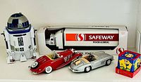 Group shot of all five items: R2-D2 bank, Safeway truck in box, two die-cast cars, tin jack-in-the-box