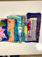 Stack of 11 folded silk scarves showing variety of colors and patterns with lot tag visible