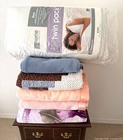 Full stack showing packaged twin pillows, blue fleece, patchwork quilt, pink and purple blankets
