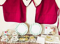 Overall lot view showing aprons, plates, teacups, runner, napkins and napkin rings