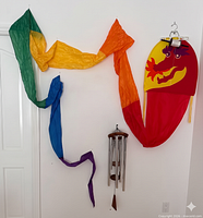 Wall display showing multicolor fabric streamer, dragon kite with tail and wind chime