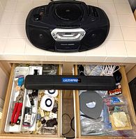 Boombox on countertop above drawers of electrical parts, LAZERPRO case visible