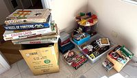 Stack of boxed board games, cardboard box with additional games, plastic bins with peg board, marbles, Pac-Man handheld, card decks