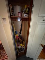 Overview of closet showing iron, paper towels, umbrellas, dusters, cleaning pole, soap pad boxes and plastic bin