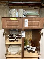 Cabinet view with Denby mugs, green plates, stacks of white plates, soup bowls, glassware and espresso cups
