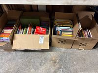 Four cardboard boxes filled with assorted books on concrete floor