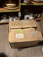 Cardboard box labeled glass, shelves with teapots, mugs, Italian basketweave ceramics, metal mixing bowl