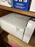 White original box containing Wolfgang Puck panini maker on storage shelf