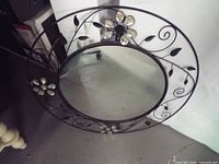 Full front view of round mirror with metal vine frame and glass flower accents
