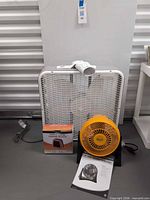Front view of all three items: box fan, boxed heater, orange turbo fan with pamphlet