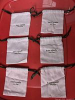 Six Kate Spade pink drawstring pouches displayed on red surface