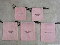 Five pink Kate Spade dust bags laid out to show front logos and relative sizes