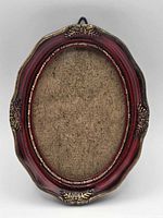 Front view of small red and gold oval resin frame with backing in place