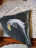 Grey and white bird with yellow bill painted on triangular slate piece, hole at top corner