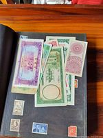 Loose assorted banknotes laid on closed stamp album showing some mounted stamps