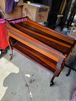 Full view of two-tier teak cart showing top and lower shelves, cabriole legs, brass casters