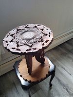 Full view of carved teak side table standing on another table