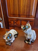 Both ceramic Siamese cat figurines front view on wood surface