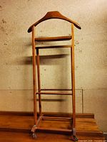 Full front view of wooden valet stand showing hanger, tray, bars and casters