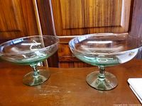 Two clear glass pedestal bowls on wood surface