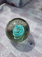Side view of glass paperweight with turquoise ribbon swirl